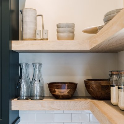 Glass containers and dishware on wood shelves in a kitchen